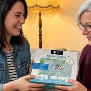 Tochter überreicht ihrer Mutter im Wohnzimmer das München-Stadtplan-Puzzle von PuzzleMap